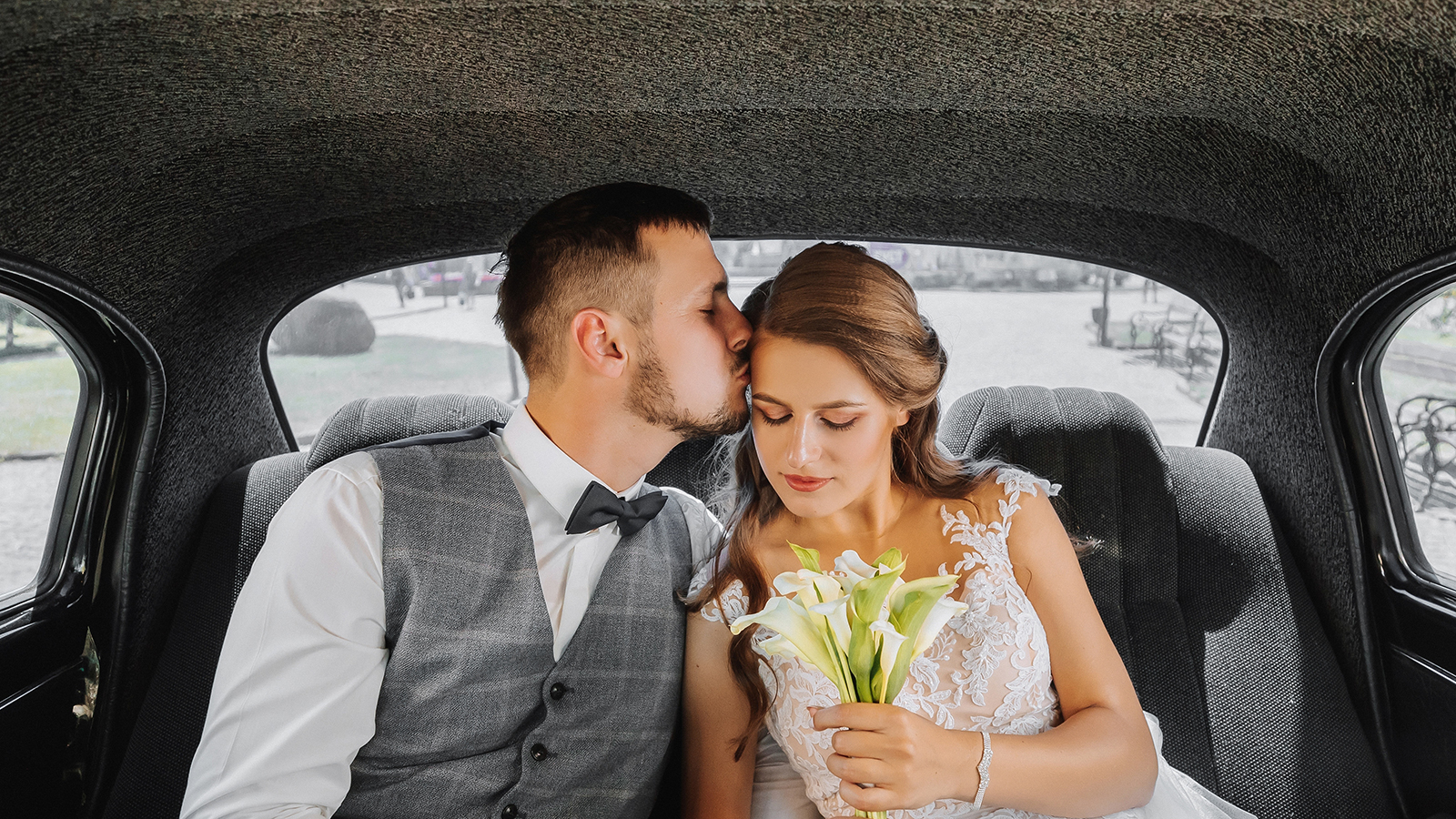 young happy bride and groom in their car rejoice and kiss after the wedding ceremony