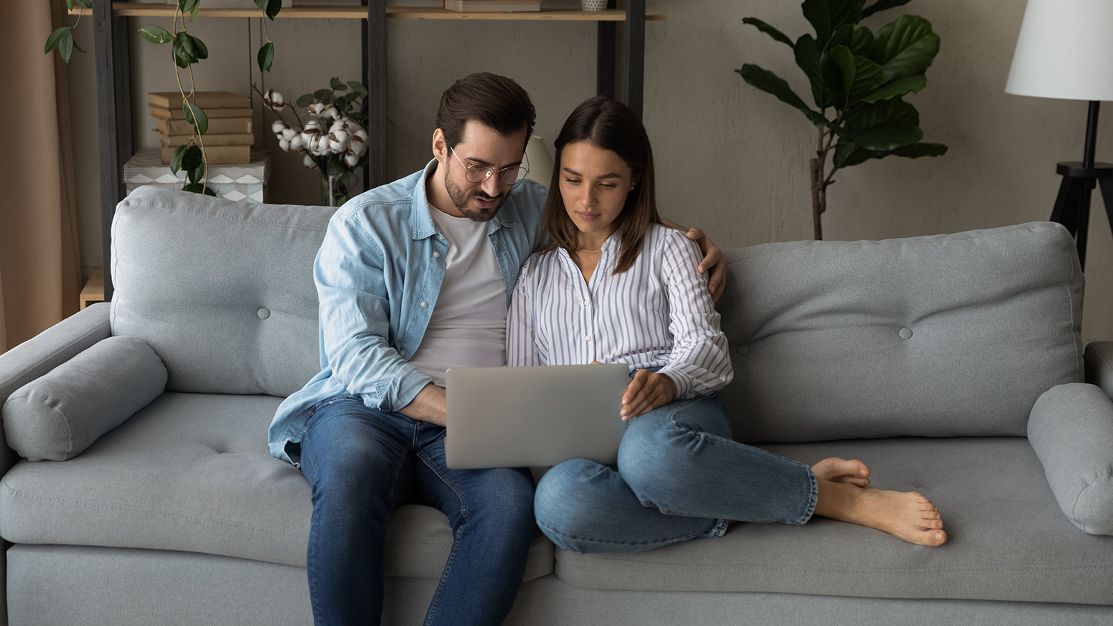 Serious young couple sit on sofa by laptop consider on making expensive purchase discuss wedding planning. Loving millennial spouses surf internet together search for new house apartment to buy rent